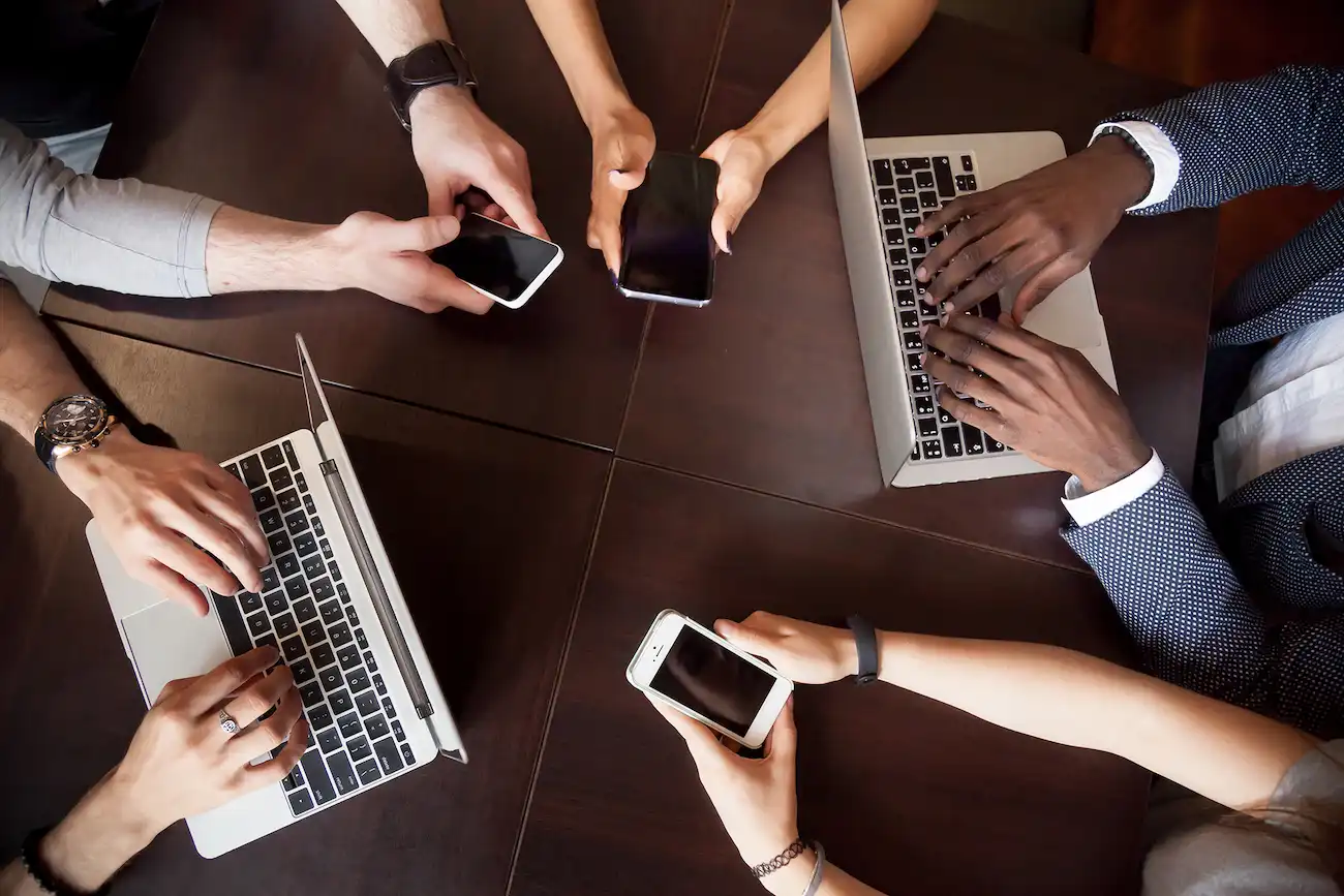 Mehrere Menschen nutzen Smartphones und Laptops an einem Tisch, um digitale Anwendungen zu testen und Schwachstellen in der Usability zu identifizieren.