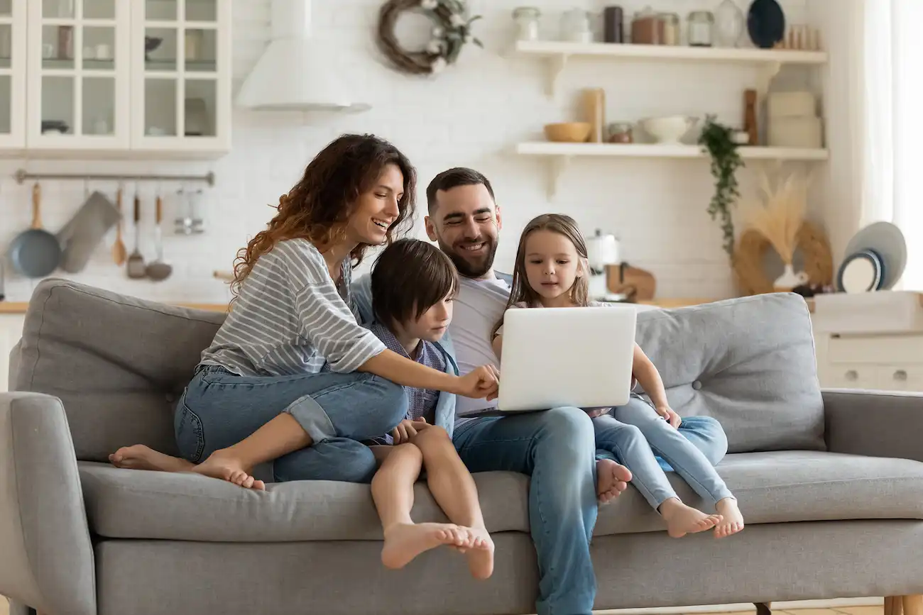 Familie sitzt gemeinsam auf dem Sofa und nutzt einen Laptop – symbolisch für die Nutzung digitaler Services durch Versicherte im privaten Umfeld.