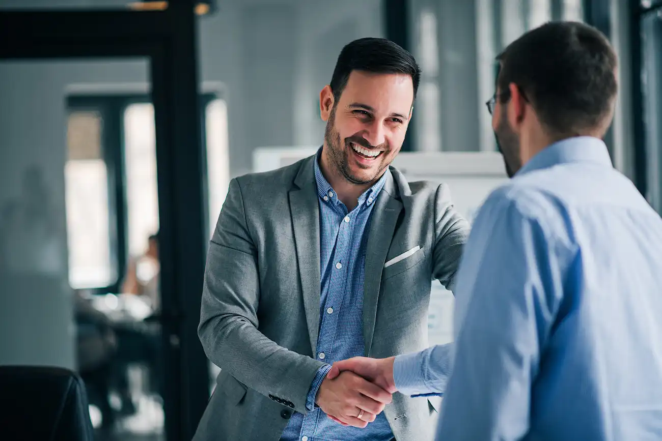 Zwei Geschäftsmänner in einem modernen Büro beim Handschlag, als Symbol für erfolgreiche Partnerschaft im Bereich Softwarequalitätssicherung und Crowdtesting.