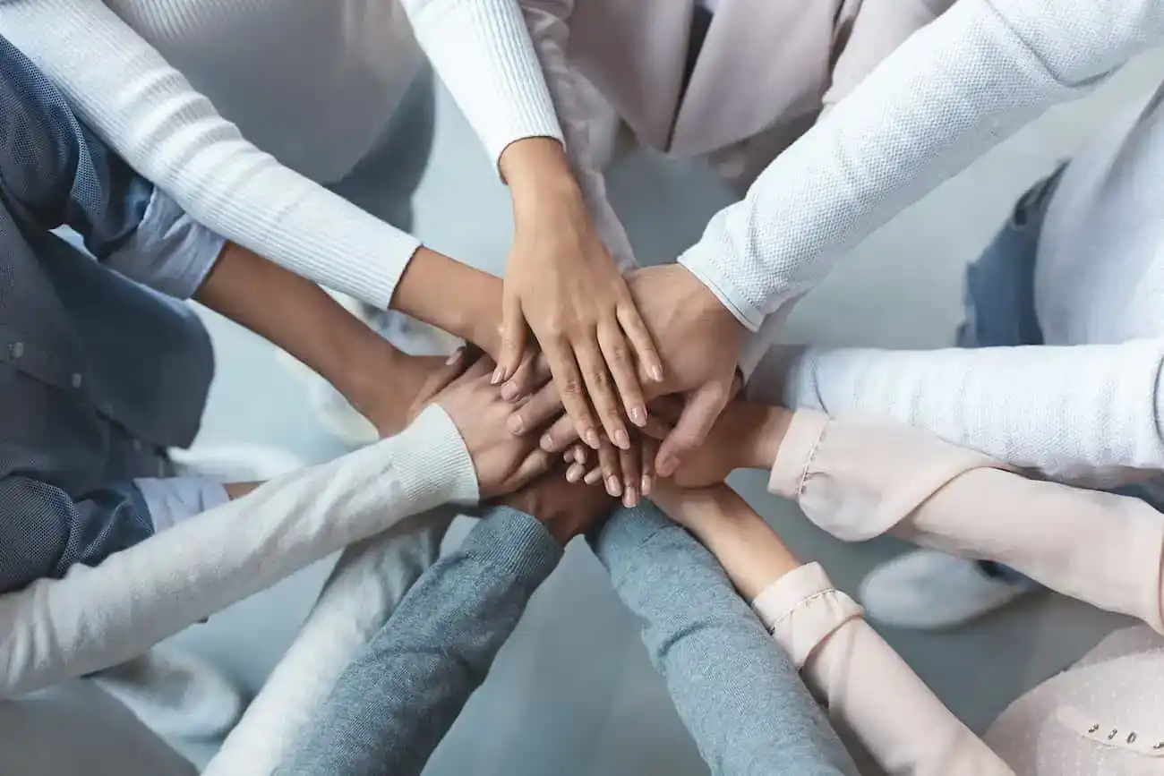 Mehrere Menschen legen ihre Hände übereinander als Zeichen für Teamwork, Vielfalt und gemeinsame Stärke in der digitalen Qualitätssicherung durch Crowdtesting.