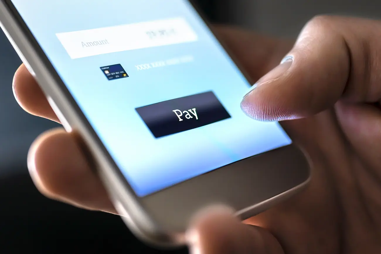 Nahaufnahme eines Fingers, der auf einem Smartphone den digitalen „Pay“-Button in einer mobilen Zahlungsmaske berührt – Symbolbild für den Checkout-Prozess im E-Commerce.