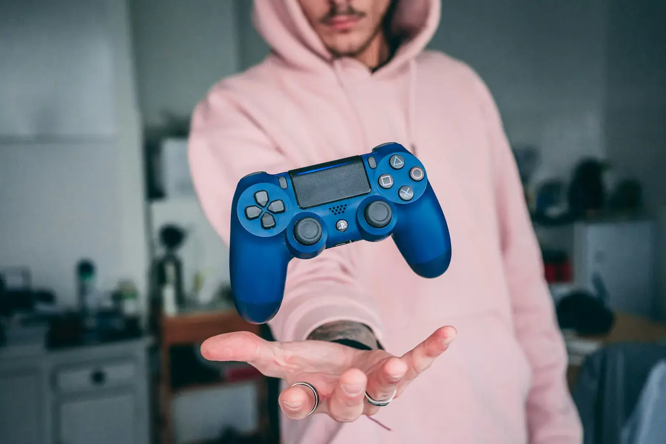 crowdtesting-gaming-qa-controller-qualitaetssicherung Person in rosa Hoodie hält die Hand aus, darüber schwebt ein blauer Game-Controller – Symbolbild für Crowdtesting, QA und Qualitätssicherung in der Gaming-Entwicklung.